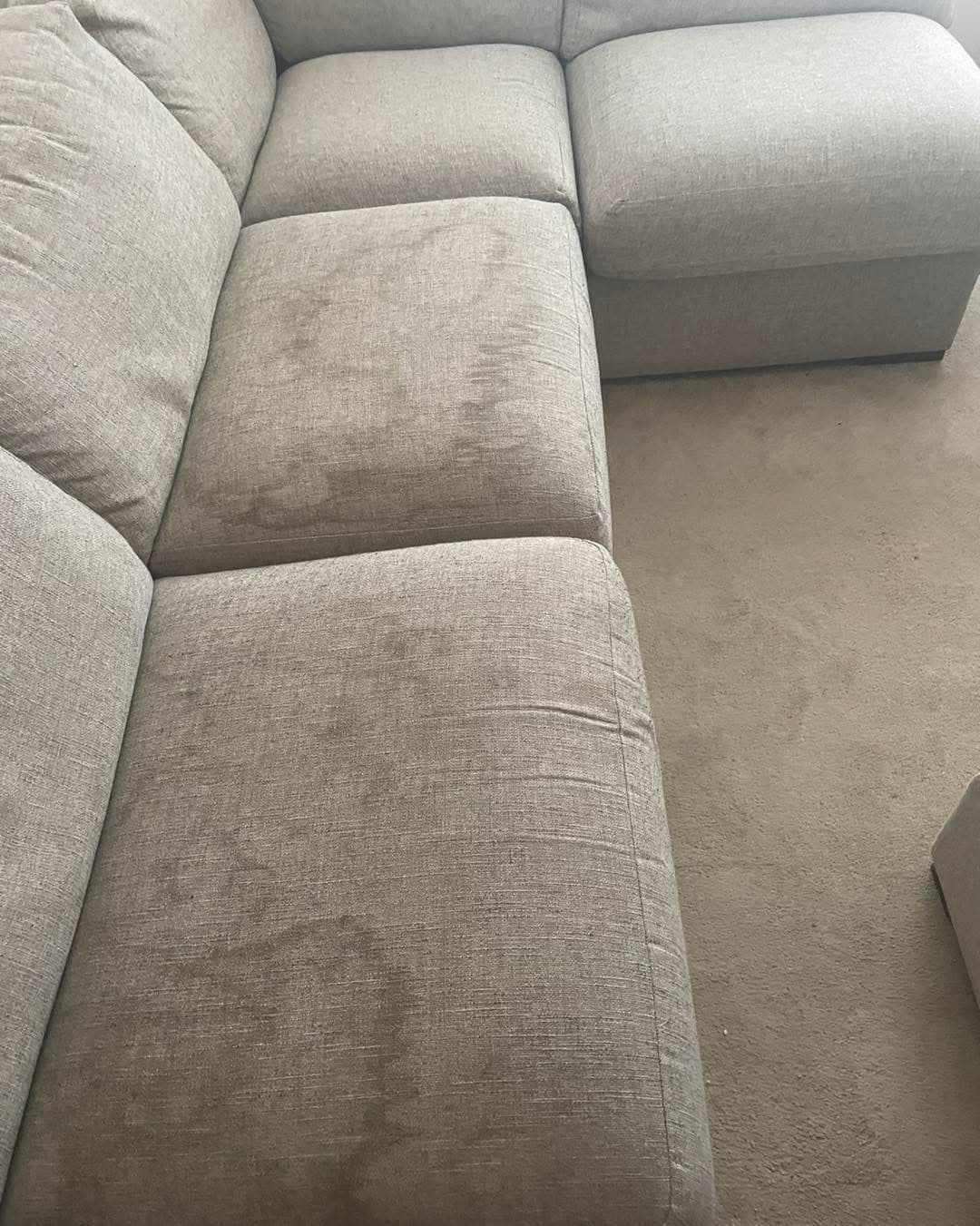 Grey L-shaped sofa with stains before upholstery cleaning